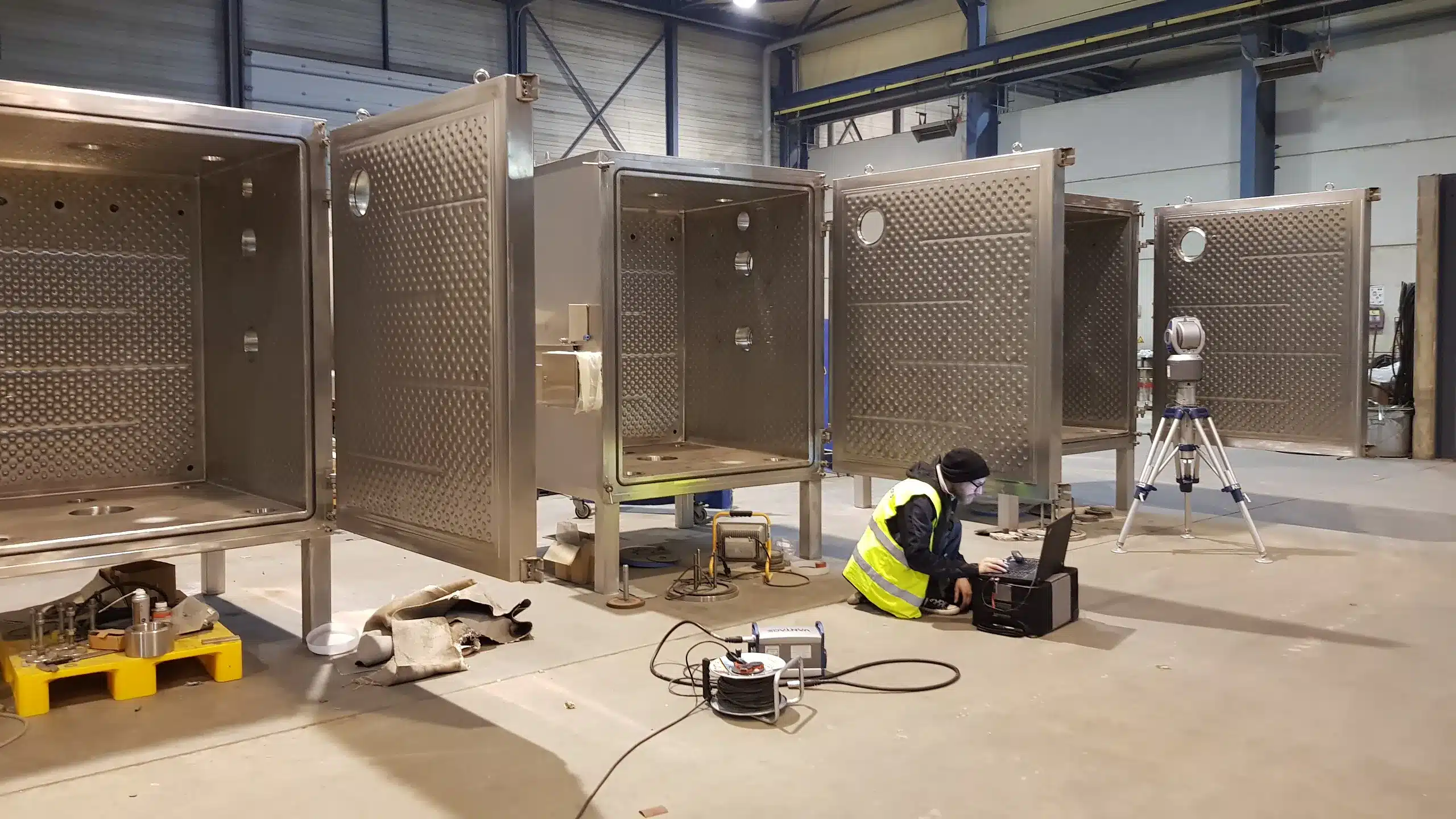 Employees measuring several stainless steel vacuum drying chambers in the production hall